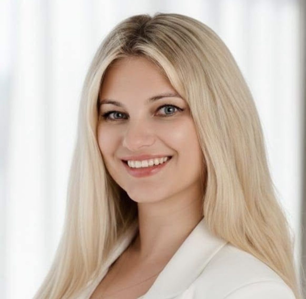 Uśmiechnięta kobieta z długimi blond włosami w białej bluzce.